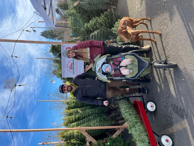 A family stands with their Christmas tree in a wheelbarrow.