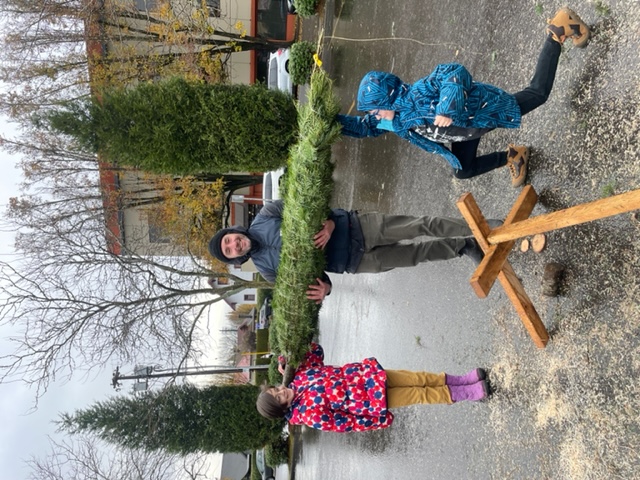 A family holds up a Christmas tree together.